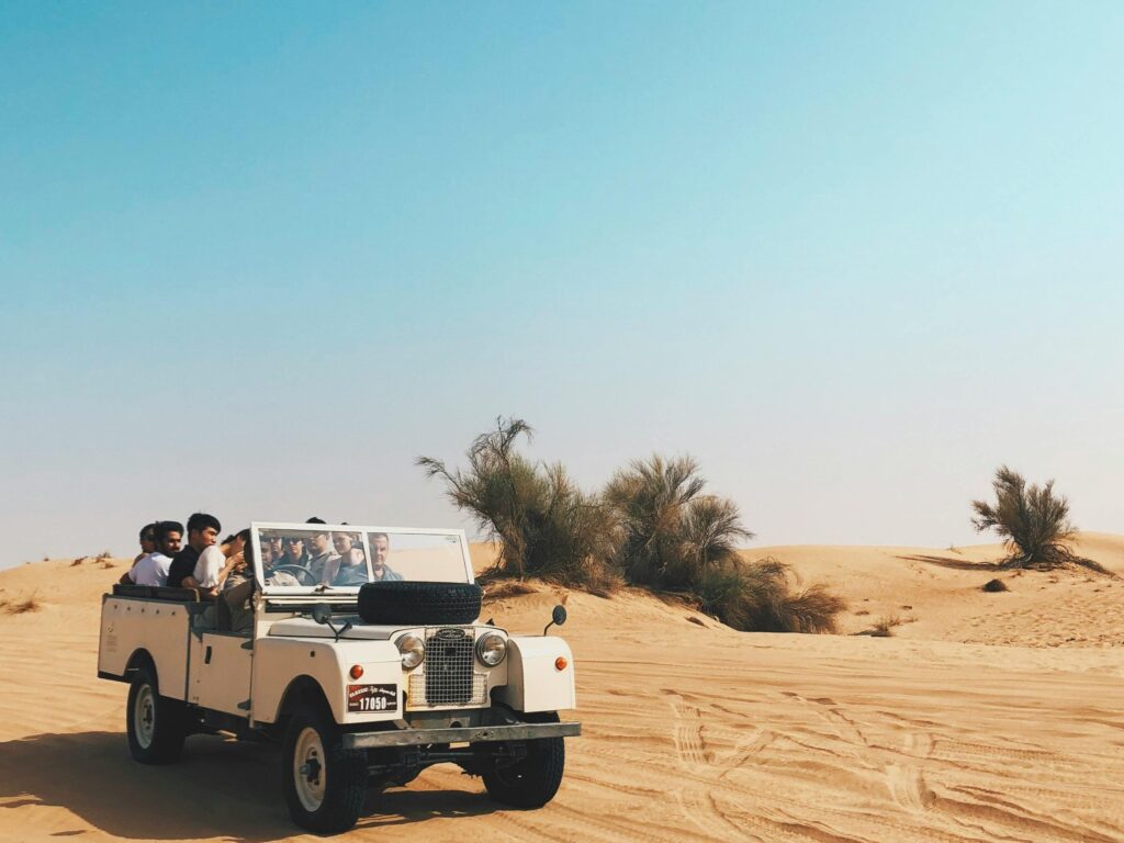 Off-road vehicle with passengers exploring scenic desert dunes under clear skies.