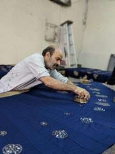 A skilled artisan applying traditional block printing techniques on blue fabric in a Jaipur workshop.